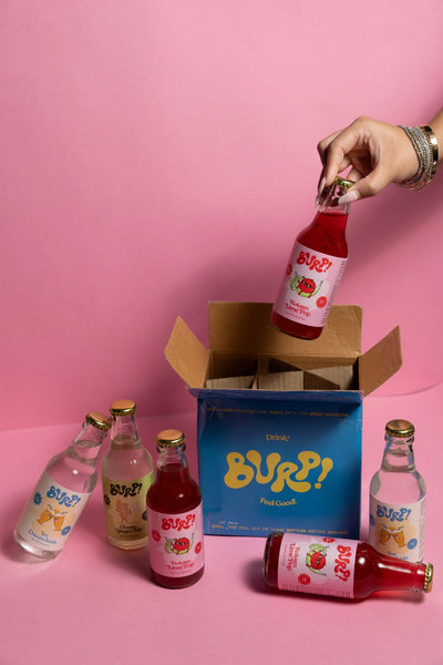 A hand holds a bottle of pink beverage above an open blue box labeled Burp!, with several Burp! drink bottles arranged on a pink background.