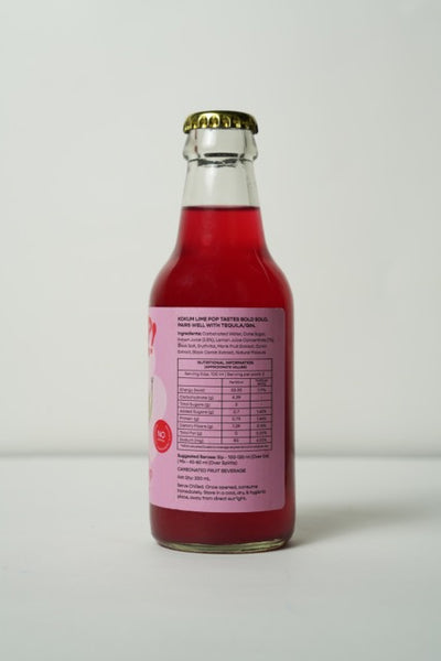 A glass bottle of Burp! Kokum Lime Pop soda, showing the back label and dark pink liquid, on a light gray background.